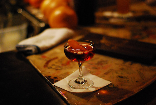 A Manhattan served with orange peel garnish in a coupe glass.